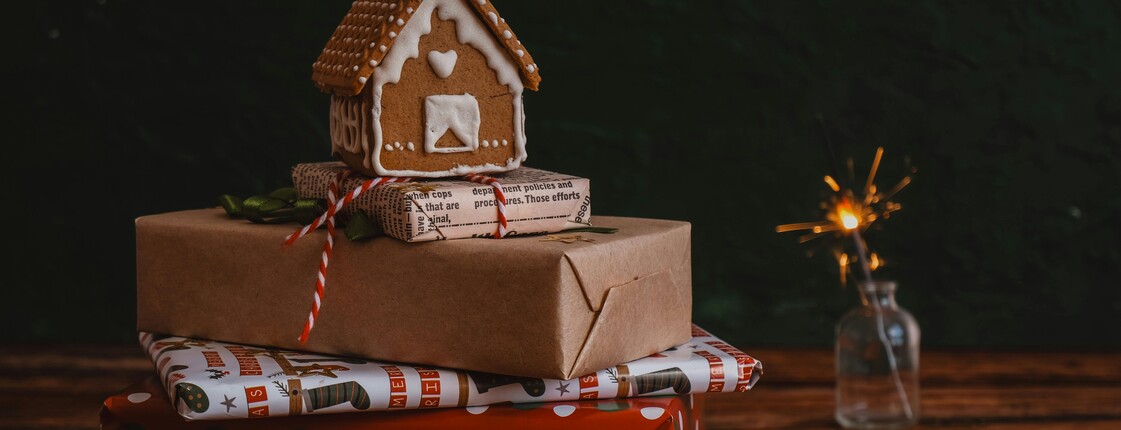Gestapelte Weihnachtsgeschenke mit einem kleinen Lebkuchenhaus oben drauf.