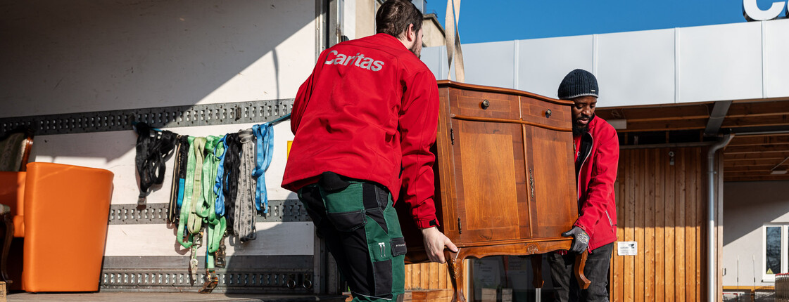 Zwei Mitarbeiter des carla Transporter laden eine Vintage Kommode aus dem LKW aus.